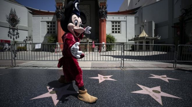 Um artista vestindo uma fantasia de Mickey Mouse em frente ao teatro TLC chinês fechado no quase vazio Hollywood Boulevard